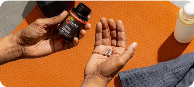 Hand holding two capsules with Cardio Capsule bottle in other hand
