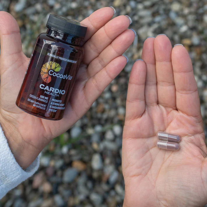 CocoaVia Cardio Capsule bottle held in one hand and the other hand holding two capsules